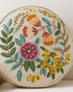 an embroidered round purse with flowers and leaves on the front, sitting on a white surface