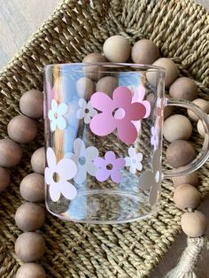 a glass mug with pink and white flowers on it sitting next to some wood beads