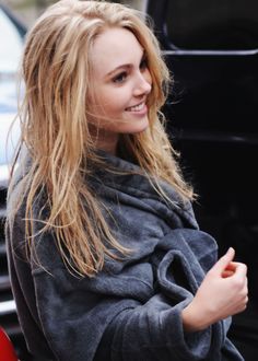 a woman with long blonde hair is standing in front of a car and smiling at the camera