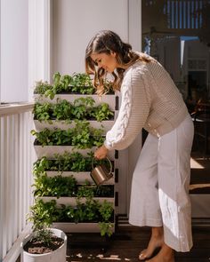 a woman is watering plants on the porch