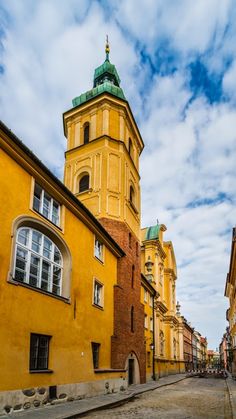 an old yellow building with a green roof and steeple on the top is next to a cobblestone street