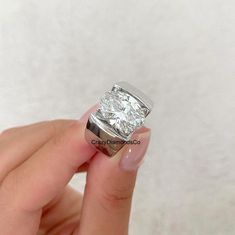 a woman's hand holding an engagement ring with a diamond in the middle, on a white background