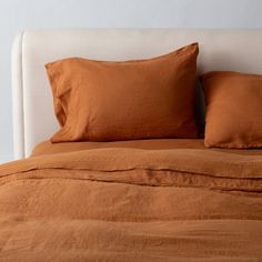 a bed with two orange pillows on top of it and a white headboard in the background