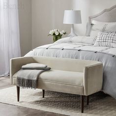 a white bed sitting next to a window with curtains on both sides and a bench in front of it