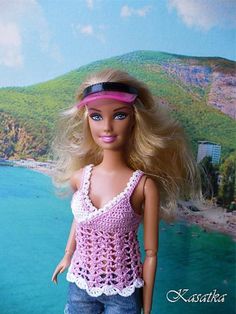 a barbie doll is standing in front of a scenic backdrop with the ocean and mountains