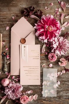 the wedding stationery is laid out with pink flowers and cards on top of it