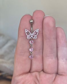 a person holding a butterfly belly ring with pink stones on the bottom and an upside down bar in the middle