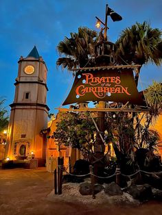 the pirate's garden sign is lit up at night in front of a clock tower