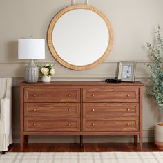 a large round mirror on the wall above a wooden dresser with drawers and vases