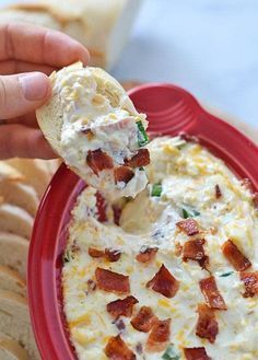 a red bowl filled with dip and bacon on top of crackers next to bread