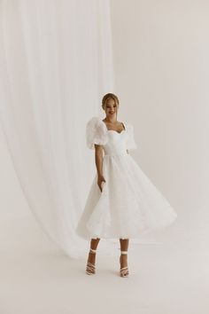 a woman standing in front of a white backdrop wearing a dress with ruffle sleeves