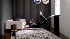 a man laying on the floor in front of a white couch and black wallpaper