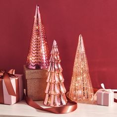 three shiny christmas trees on a table with presents