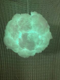 a green sweater hanging from a hook on a string with clouds in the air above it