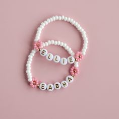 two bracelets that say believe and beaded on them in gold, white and pink beads