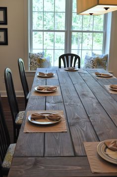 a wooden table with plates and place settings on it, in front of a window