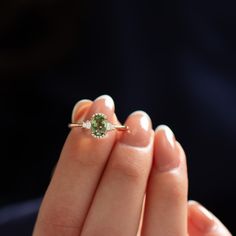 a woman's hand holding an engagement ring with a green gemstone in it