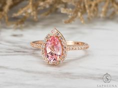 a pink diamond ring sitting on top of a white marble table next to some branches