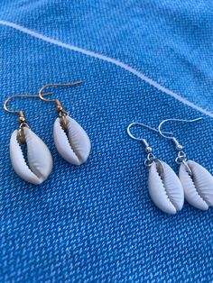 🐚- Cowrie shell dangle earrings, handmade by me. 🐚- Dainty shell dangly earrings perfect for summer and to match with the cowrie shell necklace.  🐚- A great present to send to someone, seaside theme.  🐚- Silver plated findings. 🐚- Drop earrings. 🐚- Free quick shipping. 🐚- Cute purple themed packaging. 🐚- The perfect gift, can have a gift message. White Dangle Beachy Jewelry, White Shell Earrings For Summer, White Drop Earrings For The Beach, White Dangle Earrings For Beach, White Dangle Earrings For The Beach, White Drop Earrings For Beach, Beachy Earrings For Vacation, Handmade Earrings For Beach Season Vacation, Handmade Summer Earrings For Beach Season