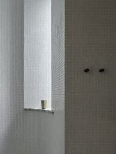 a white tiled bathroom with two black knobs on the wall and a shower stall