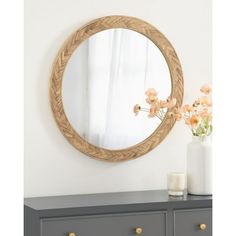 a round mirror sitting on top of a dresser next to a vase with flowers in it