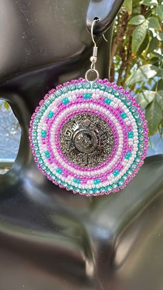 a pair of pink and blue beaded earrings hanging from a metal hook on top of a chair