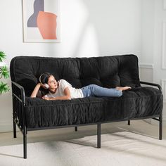 a woman laying on top of a black futon couch