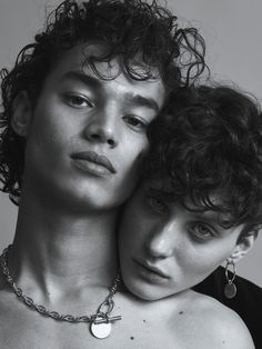 two people are posing for the camera with their heads close to one another, both wearing necklaces