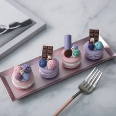 three small cakes on a pink tray with a fork and knife next to it,