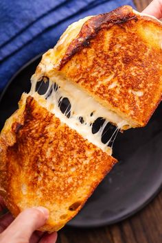 a grilled cheese sandwich being held up by someone's hand on a black plate