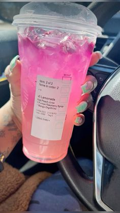 a woman holding up a pink drink in her hand while sitting in the driver's seat