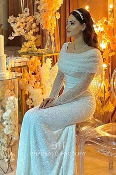 a woman is sitting on a chair wearing a white dress with long sleeves and beading