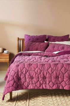 a bed with purple comforter and pillows in a pink room next to a table