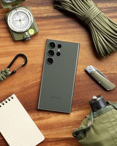 a cell phone sitting on top of a wooden table next to an army green bag