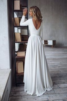 a woman in a long white dress leaning against a wall with her back to the camera