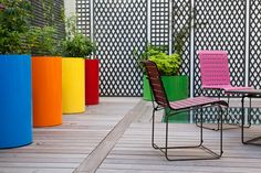 colorful chairs and tables on a wooden deck in front of a wall with vertical planters