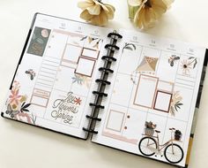 an open planner book sitting on top of a table next to flowers and a pen