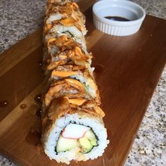 a sushi roll on a wooden cutting board next to a small cup of coffee