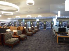 an empty library filled with lots of chairs and tables next to lamps on either side of the bookshelves