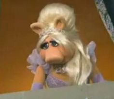 a close up of a stuffed animal with blonde hair and blue eyes wearing a purple dress