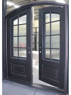 two black double doors with glass panels in an empty warehouse building, one opened and the other closed