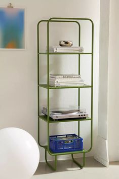 there is a green shelf with several books on it and a blue basket next to it