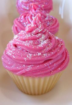 two cupcakes with pink frosting and sprinkles are on a white plate