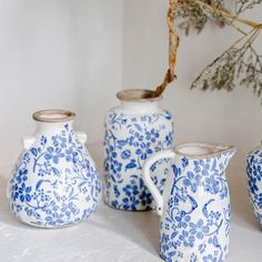 three blue and white vases sitting next to each other on a table with a tree branch in the background