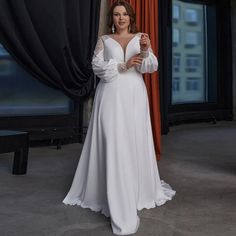 a woman standing in front of a window wearing a white dress with long sleeves and an open back