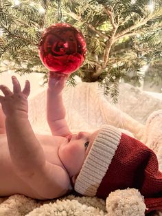 a baby laying on its back in front of a christmas tree with a red ornament