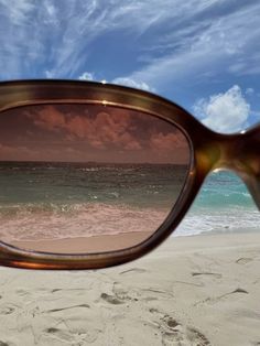 a pair of sunglasses sitting on top of a sandy beach next to the ocean under a cloudy blue sky