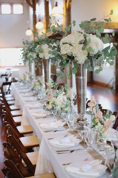 a long table is set with white and pink flowers in tall vases on the tables