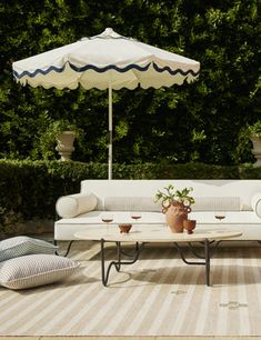 an outdoor seating area with umbrellas and potted plants on the floor, in front of trees