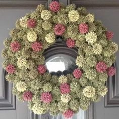 a wreath with pink and white flowers hanging from the front door on a gray door